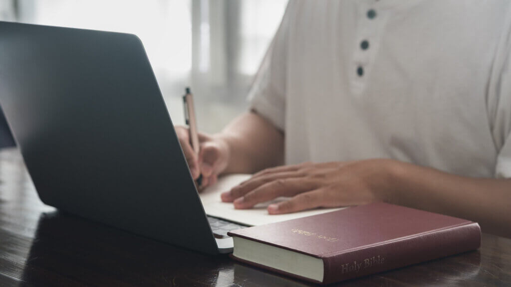 Student working on laptop with a Bible at his side